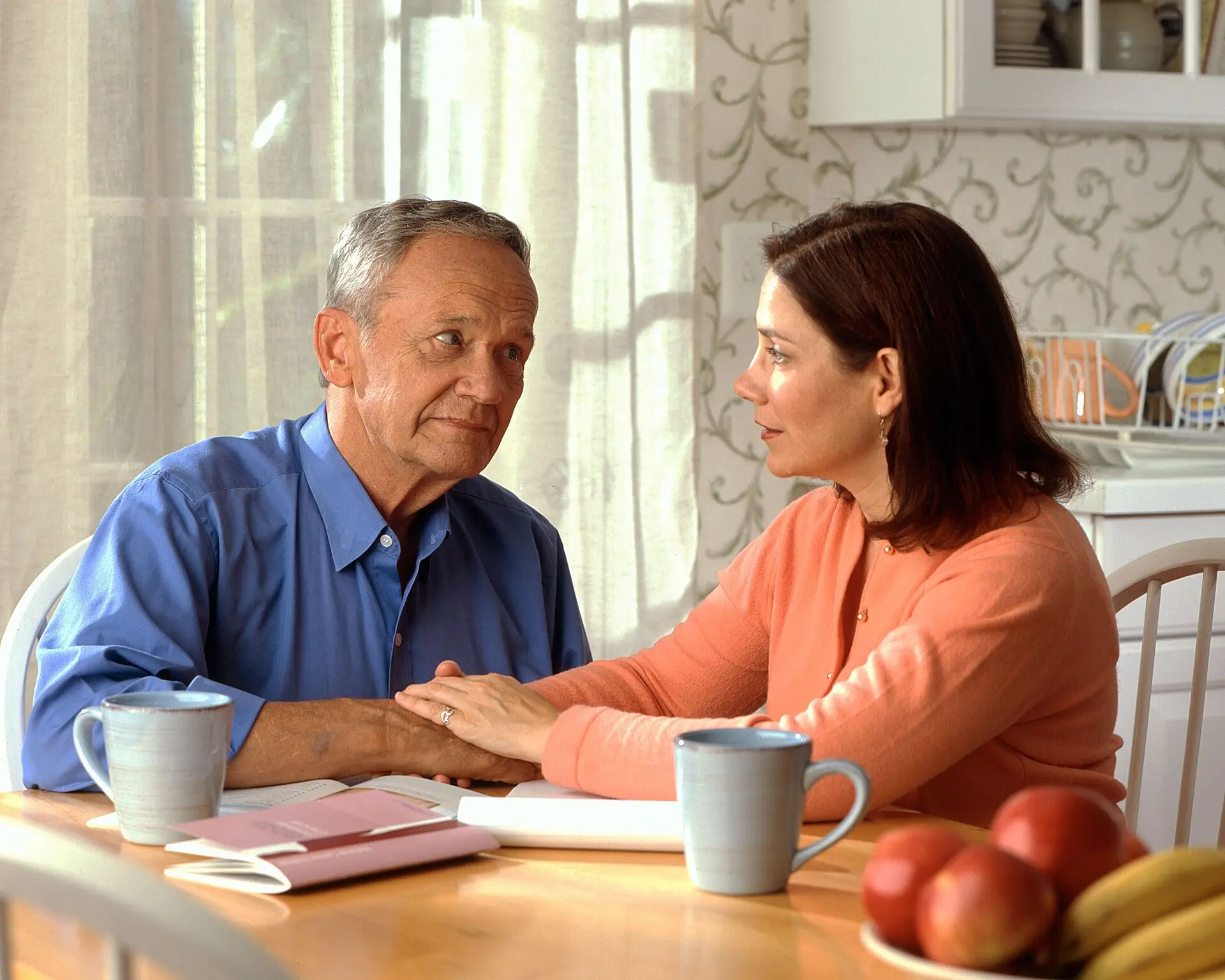 A couple talking at a kitchen table with coffee mugs and papers