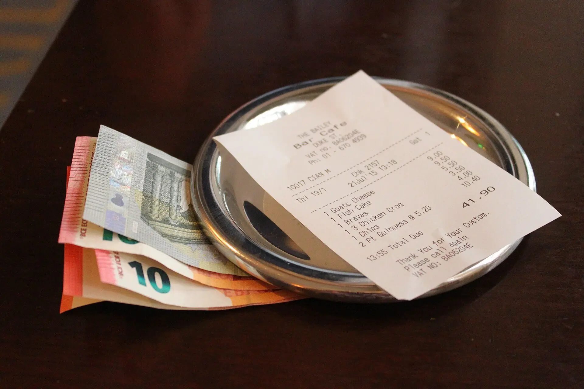 A restaurant receipt on a small metal tray next to euro banknotes